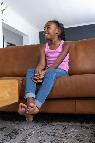 African american girl sitting on brown leather sofa smiling at home, casual family moment