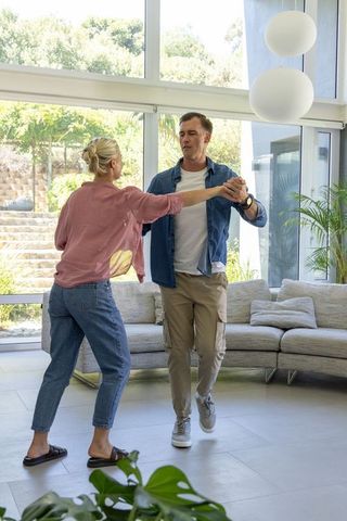 Couple dancing in bright modern living room with glass wall and garden view