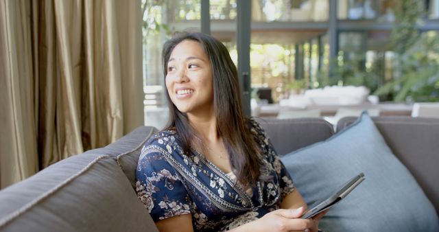 Smiling Woman Sitting on Sofa Holding Tablet in Modern Home - Download Free Stock Images Pikwizard.com