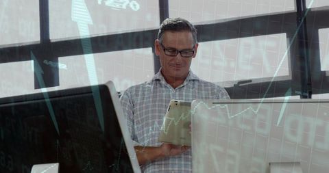 Businessman analyzing market data on tablet with financial charts overlay in modern office