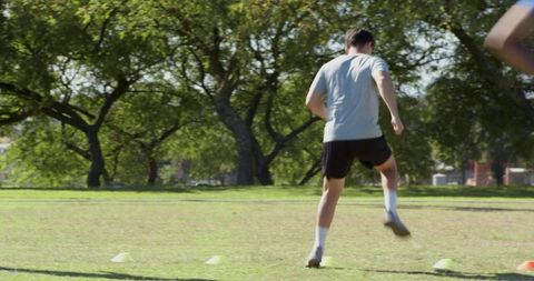Adult male performing agility cone drills in park wearing cleats and training gear