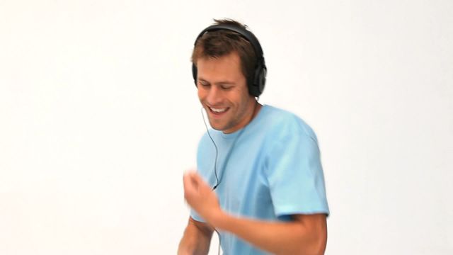 Man in blue shirt enjoying music through headset while dancing. Perfect for themes related to music enjoyment, leisure activities, lifestyle, happiness, and indoor entertainment.