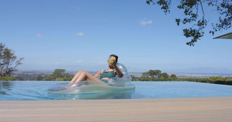 Relaxing woman floating on clear inflatable in infinity pool with city skyline view