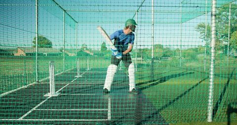 Cricketer practicing batting in outdoor net cage on sunny wicket