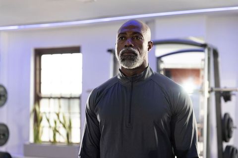 Senior african american man standing in gym wearing dark athletic pullover, focused strength and det