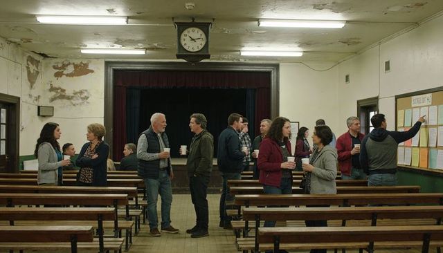 Community meeting in village hall with locals chatting over coffee among weathered benches