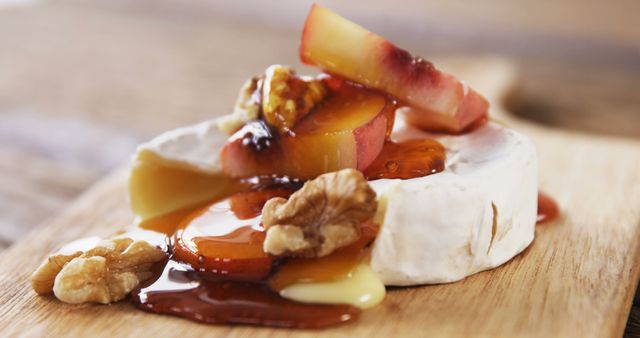 A creamy wheel of brie cheese is topped with caramelized peaches and drizzled with honey, garnished with walnuts on a wooden board. This appetizing setup suggests a gourmet experience with a focus on rich flavors and textures.