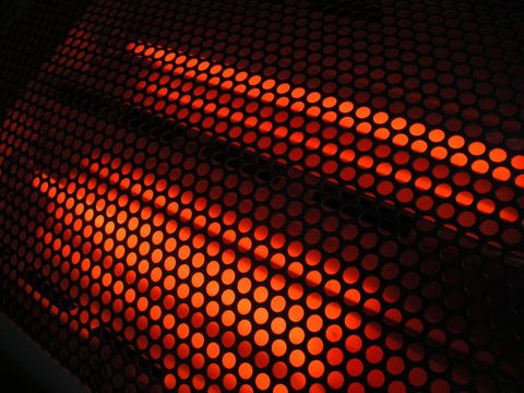 Glowing red infrared heater behind perforated metal grille creating geometric pattern