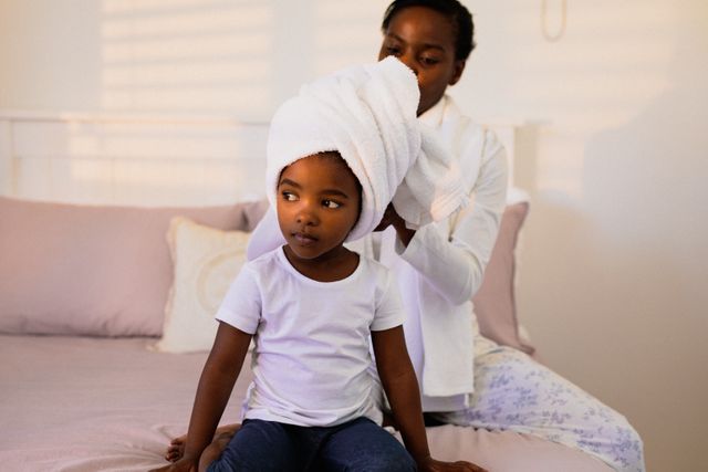 Mother drying her young daughter's hair with a towel in a cozy bedroom. Perfect for themes related to family bonding, parenting, morning routines, and home care. Ideal for use in articles, blogs, and advertisements focusing on family life, childcare, and personal care products.