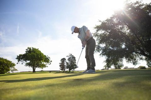 Man Putting on Sunlit Golf Course with Greenery and Trees