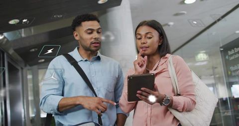 Business travelers consulting tablet in airport concourse for trip planning and collaboration