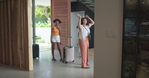 Friends arriving home with rolling suitcases in modern foyer