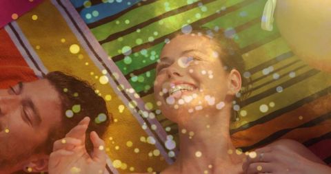 Young couple lying on colorful striped towel soaking up sun with lens flare bokeh