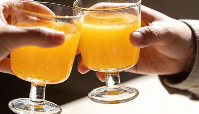 Clinking short-stem glasses filled with orange juice toasting brunch morning warmth glow
