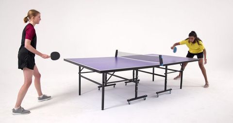 Women competing in ping pong match on purple table