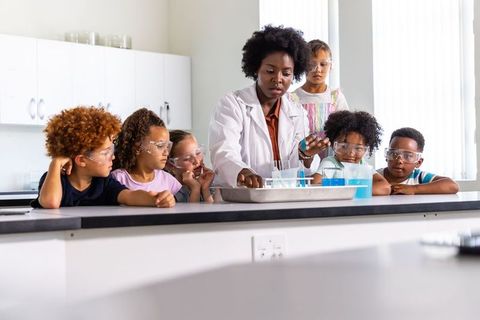 African american instructor teaching kids science experiment with test tubes and goggles