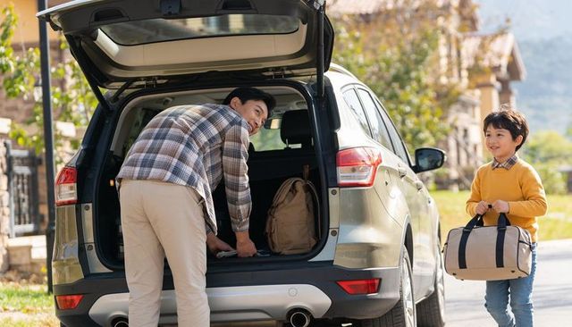 Father loading suv trunk while son carrying duffel, family packing for weekend road trip