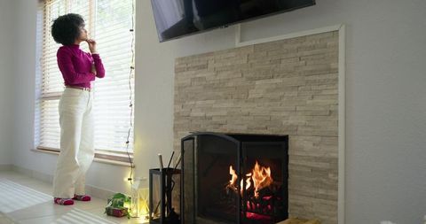 Mid-adult african american woman gazing through blinds by cozy fireplace