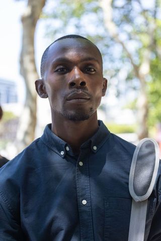 Confident african man standing in park wearing navy button-up shirt carrying padded strap