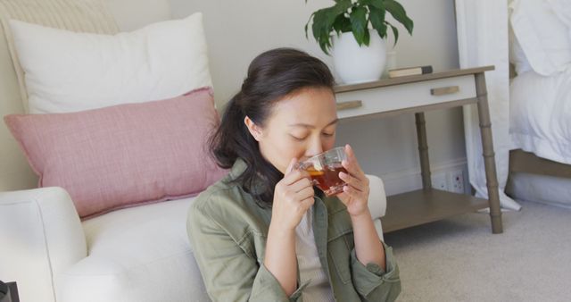 Woman sitting on floor, sipping tea in cozy home environment. Ideal for concepts including relaxation, self-care, tranquility, home comfort, personal time, and leisure activities.