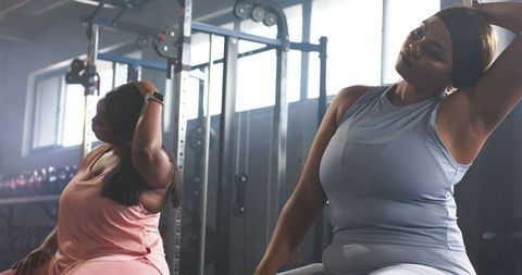 Diverse plus-size women performing seated neck stretches in gym wearing headband