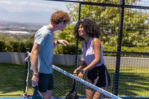 Laughing couple pointing over net on outdoor pickleball court enjoying casual match