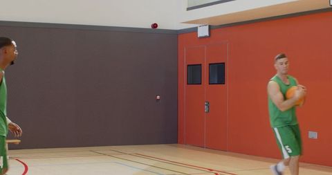 Basketball player clutching ball on indoor court with red doors for sports marketing