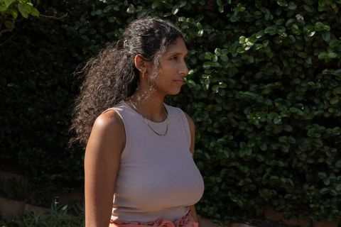 Indian woman standing in profile wearing ribbed tank and gold jewelry in sunlit garden