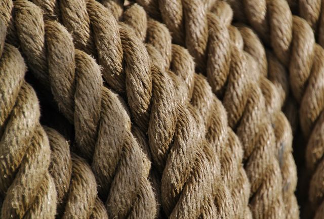 Close-up view of thick natural rope coils highlighting texture and fibers. Useful for themes related to nautical settings, rustic backgrounds, or texture studies. Ideal for design elements in crafts, maritime projects, or interior decoration.