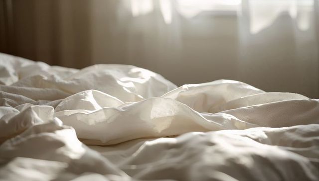 Sunlit rumpled white duvet and linen sheets soft folds, texture, warm morning light
