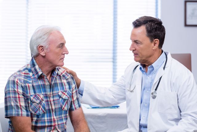 Doctor consoling senior man during a medical consultation in a clinic. The doctor is showing empathy and support, which is important in healthcare settings. This image can be used for articles or advertisements related to elderly care, medical consultations, healthcare services, doctor-patient relationships, and emotional support in medical settings.