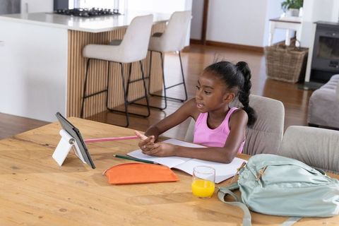 Young african girl learning at home with tablet and notebook, remote study and homework