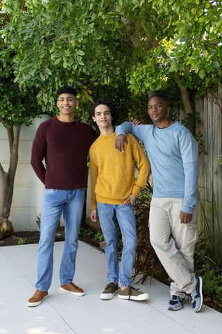 Young men standing together on backyard patio wearing sweaters and jeans