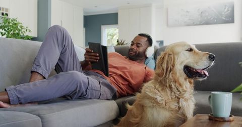 Relaxing african american man listening to headphones on couch with golden retriever