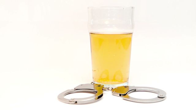 This stock video depicts a beer glass with car keys dropping into it while laying next to handcuffs on a white background. The video symbolizes the dangers and legal consequences of drunk driving. It can be used in campaigns and articles related to DUI awareness, traffic safety, law enforcement, and public health education.