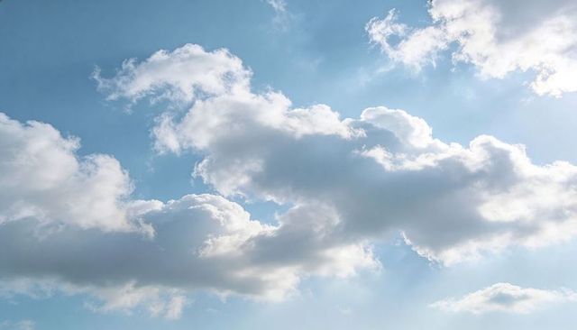 Sunlit Cumulus Cluster Drifting Over Blue Sky with Soft Crepuscular Rays and Wisps