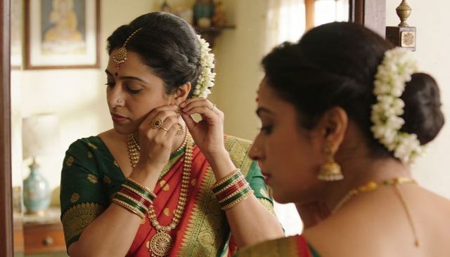 South indian bride fastening gold earring wearing green red silk saree jasmine garland