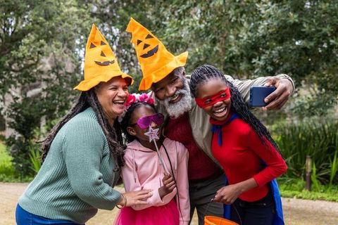 African american family taking selfie in halloween costumes outdoors with playful pumpkin hats