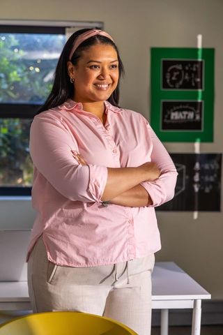Confident teacher standing with arms crossed in bright classroom with math posters