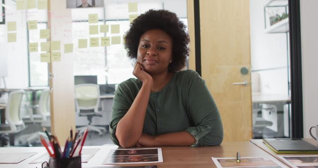 Portrait of african american businesswoman sitting at desk leaning on hand and smiling in office. work at an independent creative business.