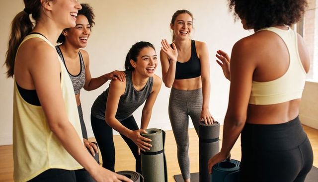 Laughing women holding yoga mats after workout celebrating wellness, community, friendship