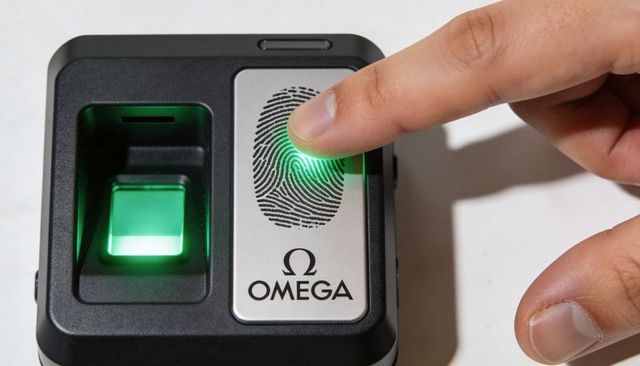 Pressing finger on biometric fingerprint scanner with green led and omega logo for secure access