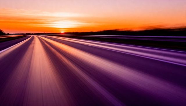 Highway at sunset showing speed motion blur and purple light streaks on asphalt road