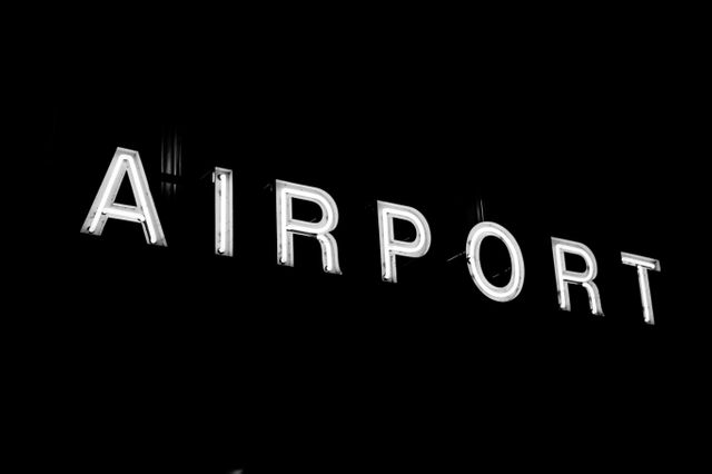 Illuminated 'Airport' sign standing out against a black background, creating a stark contrast. This image can be used for travel-related promotions, airport advertisements, or presentations focused on air travel and transportation. Ideal for businesses in the travel industry or for aesthetic, modern design projects.