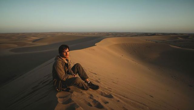 Traveler sitting on sand dune crest at golden hour embracing desert solitude