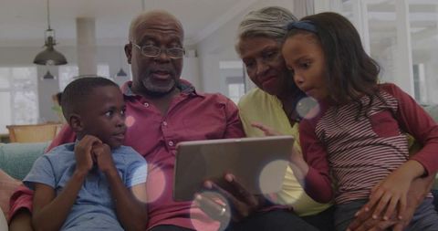 Grandparents sharing tablet with grandchildren on sofa, multigenerational family bonding