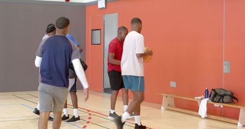 Young men walking across indoor basketball court carrying ball and bags after practice
