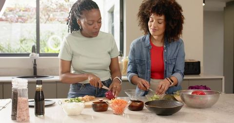 Diverse women chopping vegetables on marble kitchen island preparing healthy meal
