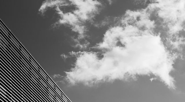Image showcasing the sharp angles of a modern building against a backdrop of clouds, captured in black and white. Ideal for projects focusing on architecture, urban design, simplicity, and contemporary art themes. Can be used in blogs, presentations, and marketing materials highlighting modern architectural techniques and minimalist aesthetics.