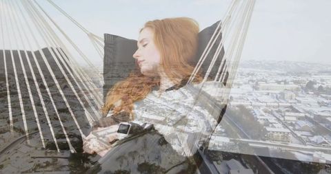 Red-haired woman relaxing in hammock holding smartwatch, phone double exposure snowy cityscape